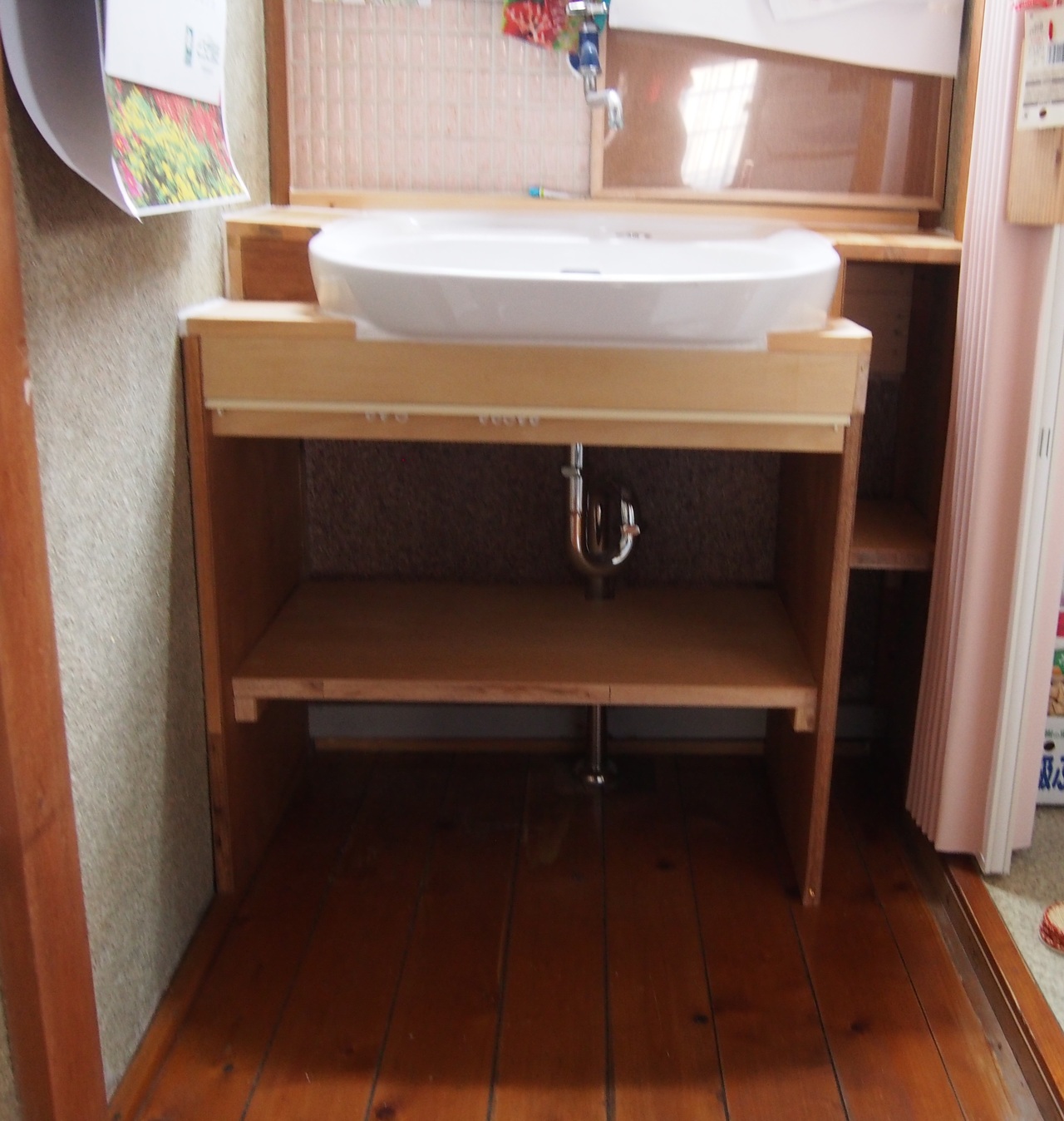 洗面台に合わせて棚を作りました。 左上の棚が微妙に斜めになっているのは、水はけを良くするため。 間口いっぱいにしてしまうとトイレの入り口と干渉してしまうので、 シュミレーションをしながら余すところなくスペースを活用しました。 手前にはお客様が好きな柄のカーテンを付けたいとおっしゃっていたので、 カーテンレールを付けました。